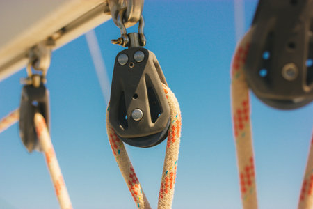 Ship block with ropes. Steel sling and rope clamp connected by screw bolt. Device for adjusting the tension or length of ropes on the deck of a ship, yacht. boat parts. Roller blocks against blue sky.の写真素材