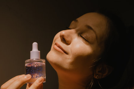 A beautiful young woman holding cosmetic bottle serum in hand A pleasure of facial skin care. beauty and youth concept. Warm filter portrait close-up with satisfied girl's face dreaming closed eyes.の写真素材