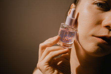 A beautiful young woman holding cosmetic bottle serum in hand A pleasure of facial skin care. beauty and youth concept. Warm filter portrait close-up with satisfied girl's face dreaming closed eyes.の写真素材