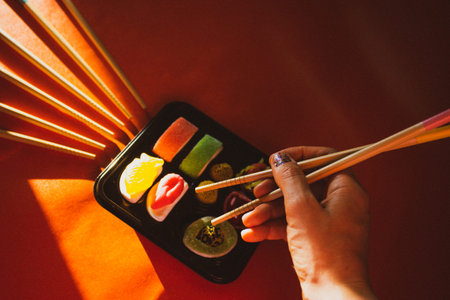Wooden sushi sticks chopsticks in female hand eating jelly candies Sushi set in a plastic black box on bright red background Asian Japanese Chinese food. Sweet food with candies. elegant food photo.の写真素材