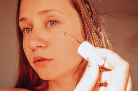 Beautiful white European baby dace young woman portrait close-up applying face serum from an eyedropper. Intense facial skin care cosmetic. Daily routine and self-care. Women's beauty tools products.の写真素材