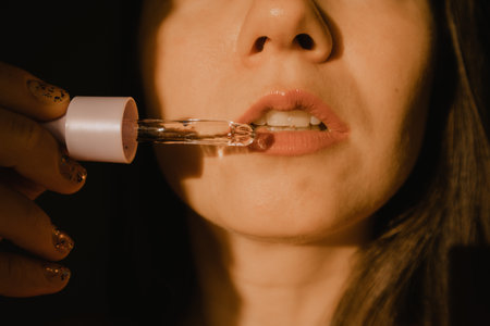 Moisturizing lip skin. Beautiful white young woman portrait close-up applying face serum from an eyedropper. Intense facial skin care cosmetic. Daily routine, self-care. Women's beauty tools products.の写真素材
