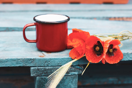 Still Life with a red coffee or tea cup and a bouquet of red poppies on a wooden blue surface. Gathering wild spring flowers in a garden. Rural scene. Vintage retro spring nature background. Nostalgiaの写真素材