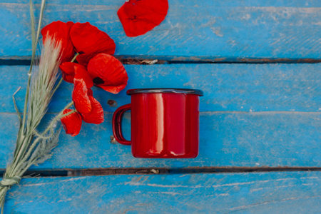 Still Life with a red coffee or tea cup and a bouquet of red poppies on a wooden blue surface. Gathering wild spring flowers in a garden. Rural scene. Vintage retro spring nature background. Nostalgiaの写真素材