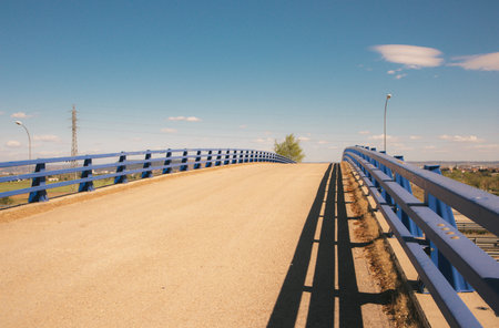 Overpass bridge against blue sky. Asphalt paved road, metal guardrails at midday. Travel in warm summer sunny day. Straight pathway goes over a horizon. no people. Rural street scene. infrastructure.の写真素材