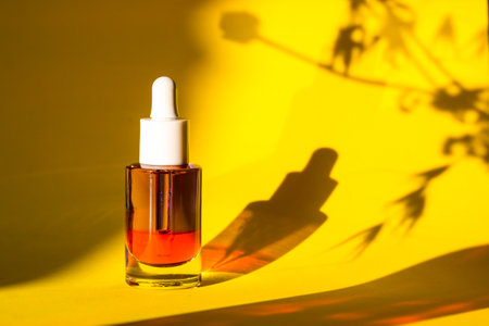 Glass cosmetic jar with serum for face and body skin care on yellow background. Grooming cosmetics for women. Female beauty tool and cosmetic. Face serum on natural backdrop with plants shadows.の写真素材