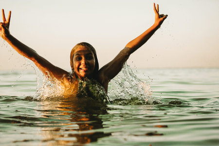 A happy little girl frolicking in the water in summer. A teenager on summer vacation swimming, jumping in the river, lake, sea, ocean. Active recreation in nature at the children's camp. peace fingersの写真素材