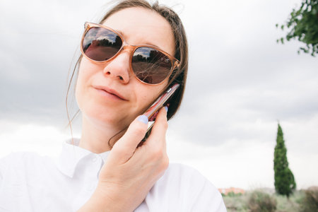 Young business woman holding a cell phone in hand talking by telephone in a city park. A happy...
