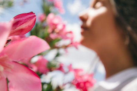 A young beautiful woman in a defocused background of pink flowers on a blooming oleander shrub. The girl is sniffing the flowers enjoying the fragrance. Abstract background of a human on nature.の写真素材