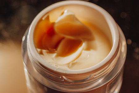 Face cream in a round jar on a dark background view from above. Feminine beauty, grooming, facial and body skin care concept. Golden body lotion with a soft texture selective focus. spa treatments.の写真素材