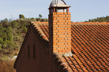 Brick chimney to vent smoke from stove, fireplace. Red-brown tile roof and chimney on the roof oa private residential house Concept of heating with wood in old houses. Clay, ceramic, concrete roofing.の写真素材