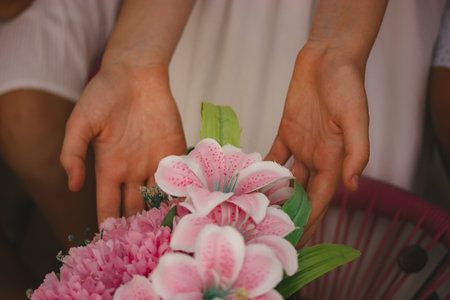A beautiful bouquet of pink flowers, lilies in the bride's bouquet in a woman's hands. A girl touching a bunch of pinky tropical flowers in bloom in spring garden. Elegant wedding flora. Romantic ceremonyの写真素材
