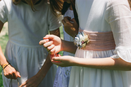 Three little girls - bridesmaids - in classic white dresses with ribbon, flowers. Girlfriends share secrets. Girlishness, tenderness, childhood. A child, friends are looking at something in the hands.の写真素材
