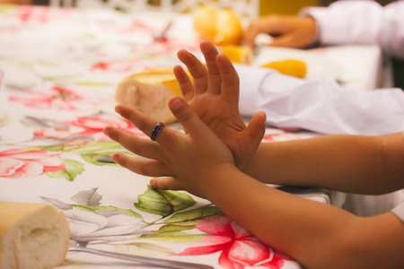 Children sit at a table with their hands on a floral tablecloth and wait for food to be served. Hungry kids at a banquet for weddings, christenings in a restaurant. People have breakfast, lunch.の写真素材