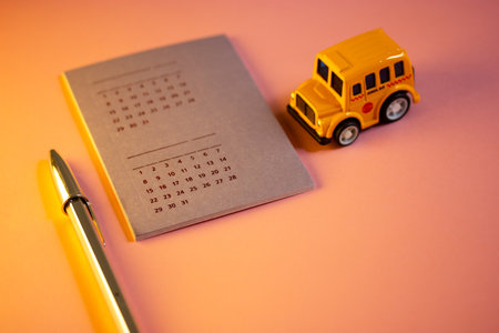 Madrid, Spain. August 1, 2022 Toy school bus, calendar with different dates, shiny pen - stylish study tools on pink background in warm light. Back to school university in September Studying scheduleの写真素材