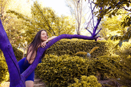 Beautiful young brunette woman posing near purple tree hugging gently a trunk. Girl on a walk in the park, forest. Traveling through nature reserves. Unusual creative exhibition in landscape design.の写真素材