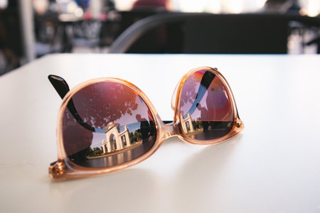 Brown stylish female sunglasses lying on a surface of a white table on a terrace of a cafe, restaurant. Sunny hot weather on a summer day. Concept of rest, vacation in summertime.の写真素材