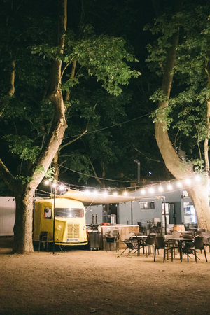 Madrid Spain. July 7 2023 Platform near a food truck with tables and chairs. Fast food on a city street. Urban space, area in evening park with garlands for eating. Summer festival in a park, forest.のeditorial素材