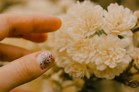 Creamy yellow miniature roses, fragrant buds in female hand. Woman touching flowering buds on shrub in a spring summer garden. Floral greeting card. Roses on a twig, branch on green natural backgroundの写真素材