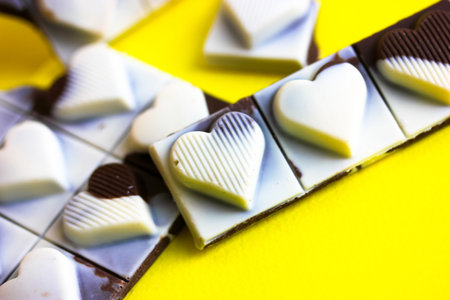 Milky dark chocolate bar with hearts on each slice top view. Broken black white pieces on yellow...