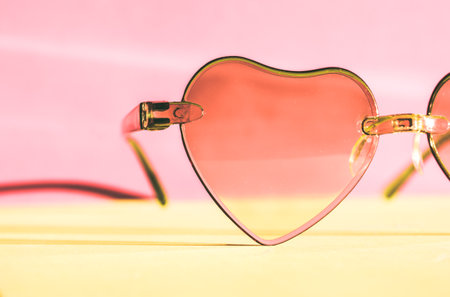 Sunglasses with pink glasses in the shape of hearts on a pink yellow pastel background. Fashion accessories for summer vacation. Female beauty accessory. Summertime fun, travel concept Valentine's Dayの写真素材