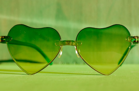 Sunglasses with green glasses in the shape of hearts. Fashion accessories for summer vacation. Female beauty accessory, glamor object. Summertime fun, travel concept. Valentine's Day. Fall in love.の写真素材