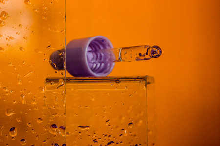 Hyaluronic acid in a glass bottle with a pipette on an orange background against wet glass. Facial Serum or cuticle oil in a bathroom. Hydro boost serum provides active moisturizing for aging skin.の写真素材