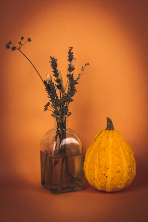 Stylish autumn still life with glass vase of wild dried flowers, pumpkin. Thanksgiving, Halloween concept Beautiful bouquet in interior. Autumn orange vintage wallpaper. Fall season vertical photo.の写真素材