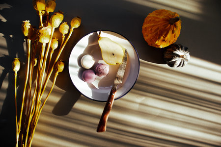 Still life with fruits in cozy interior. Plate with pear, macaroons, pumpkins on a table. Rustic...