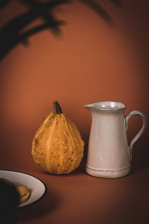 Rustic still life with a white water and milk jug next to a pumpkin on an orange background. Halloween table concept. Aesthetic composition with utensils for food preparation A glass vase with flowersの写真素材