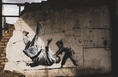 Borodyanka, Ukraine. May 1, 2023 Graffiti painted by Banksy on destroyed buildings. Boy throwing man in judo form drawing on wall. Place of mass murder of civilians by occupying russian troops in war.のeditorial素材