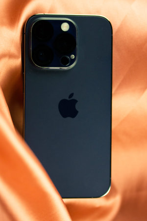 A blue smartphone iPhone 14 PRO back side view on a silk orange tablecloth.