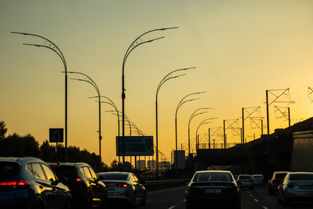 Kyiv, Ukraine October 5, 2023 A road going away with a movement of many cars at sunset. Yellow sky, sun goes down, twilights. Silhouettes of street lamps, automobiles in traffic jam with red lights onのeditorial素材