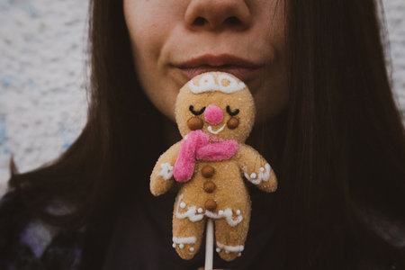 Homemade traditional Christmas cookie from dough with icing in female hand. A young woman eating a hand made gingerbread man cookies with a pink scarf. New Year 2024 doll, toy, sweet. Wintertime.の写真素材