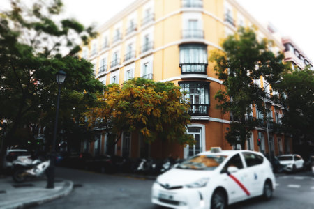 A white cab drives along a city road on an old street with classic Spanish architecture. Public transportation, services of transportation of people. Big city lifestyle. Urban scene selective focus.の写真素材