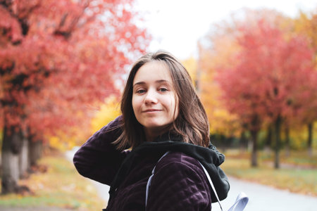 Self confident school girl on a street. Red trees in fall season Young woman portrait outdoors in...