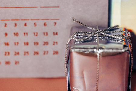 Silver shiny gift box against violet calendar background. Holidays greetings concept. Merry Christmas and Happy New Year 2024. Present wallpaper. Celebration holiday days Sales in Black Friday conceptの写真素材