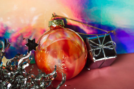 Christmas balls on abstract background. Bright orange glass glitter Christmas tree ball toy, small silver gift box on multicolored gradient background. A card for New Year's Eve 2024, Christmas Day.の写真素材