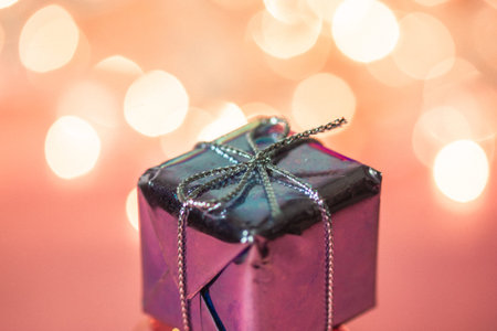 Small silver pink gift box on warm gradient background and spot lights. Holidays greetings. Merry...