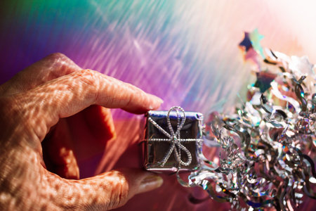 A silver gift box in a hand on pink background top view. Giving a present, congratulation with winter holiday, New Year, Christmas festive decor.の写真素材