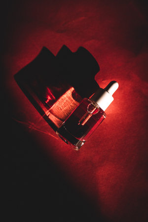 Glass cosmetic pipette bottle on red background top view. Contrasting shadows and decorative cosmetics. Facial serum dark key photo. Fashion magazine.の写真素材