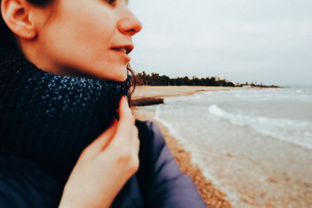 Portrait of a beautiful young smiling woman in profile by a sea in winter day. Close up female portrait on a beach shore, cold weather. Seaside travelの写真素材