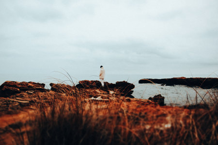 Young woman, girl in white fur coat and pants old luxury style back view standing on a seashore, ocean in cold stormy weather. Traveling to the edge.の写真素材