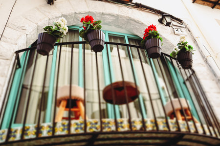 Beautiful semicircular turquoise balcony with blooming red, white flowers in flower pots. Cozy garden on terrace. Place to relax at home. White houseの写真素材