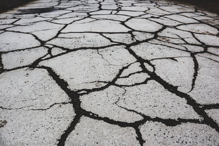 Cracked asphalt top view. Dry mud with black cracks. Gray ground background top view. Global warming problem, disaster. Aftermath of the earthquake.の写真素材