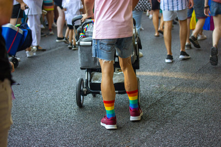 Madrid, Spain, July 1, 2022 A young father in striped rainbow socks with a stroller with his newborn baby in a gay parade. Modern people lifestyle.のeditorial素材