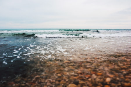 Abstract blurred natural background with blue stormy sea, ocean. Waves roll up on a shore, sandy rocky coastline. Nautical backdrop. Dreamy seascape.の写真素材