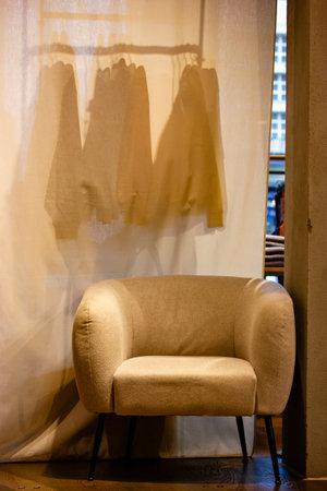 Indoors interior of a beige fitting room in a brand clothing store, shop. Elegant fashion lifestyle. A room for changing clothes with a white armchairの写真素材