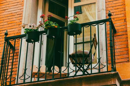 A balcony decorated with potted plants and blooming flowers. Plant-pots for home exterior decor. Place for relax, lounge space outdoors of red house.の写真素材