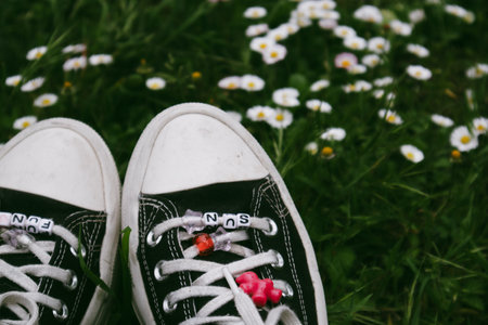 Madrid, Spain. 7 January 2024. Classic Converse sneakers on womens feet. Vintage shoes and green grass. Nostalgia for 90s. A girl relaxing in forest.のeditorial素材